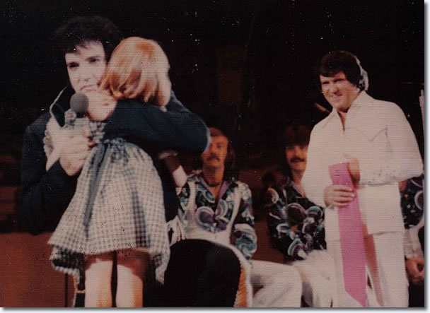 Elvis hugging a young child - who is blind. When Elvis realised she couldn't see, he kissed his scarf and touched both her eyes with it.