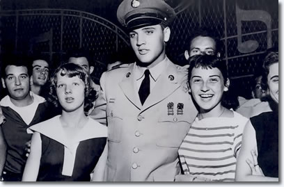 Jo Ann Mullins (Left) and Tudy Harrison (Right) greet singer Elvis Presley at the gate to his home. Presley made his first public appearance here since he started a two-week furlough on completion of basic training in the Army.