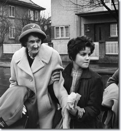 Elvis Presley's grandmother Minnie Mae Presley being led to her car by the singer's 16-yr-old girlfriend Priscilla Beaulieu in front of his house as she prepares to see him off on plane for his return to the US.