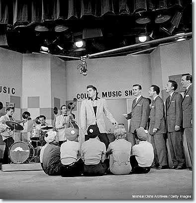 June 1956: This is also an Earl Leaf shot. It's the only time I have ever seen Elvis with his trio -- Scotty, Bill and D.J. -- and the Jordanaires all in the same shot. To me, that's just totally unique. And then you throw in the general feel of the extras -- the girls sitting there -- and the fake Colony Music Shop background. But the key thing is that I've never seen all of them together in one picture. 