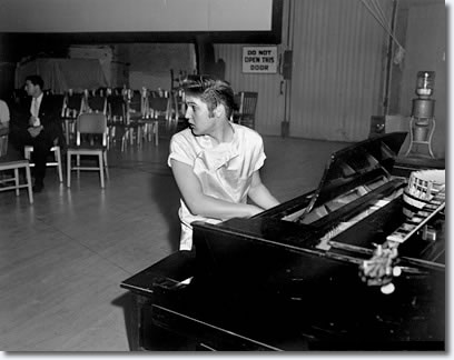 August 1956: This is during 'Love Me Tender' -- this is Elvis the first time he ever recorded without his usual musicians. He's at the 20th Century Fox soundstage studio. There's the novelty of him playing piano, which one seldom sees. Here he is in a whole new milieu -- he's in L.A. There's an openness and yet a startledness and a freshness about this shot.